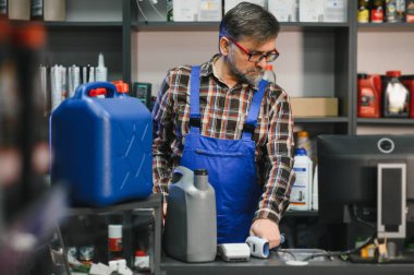 Satış elemanı otomotiv malzemeleri ile dolu raflarla çevrili bir oto yedek parça mağazasının tezgahında motor yağı ve çeşitli ürünleri tarıyor.
