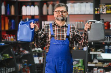 Bir oto yedek parça mağazasında müşterilere yardım ederken iki kutu motor yağı tutan tamirci, otomotiv ürünlerinde uzmanlık gösteriyor