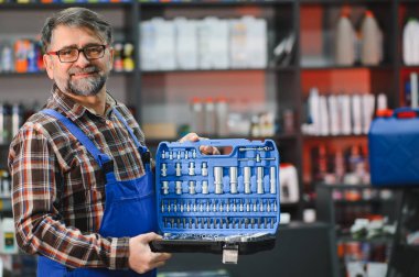 Bir oto yedek parça mağazasında araç gereç satan kıdemli bir satıcı, araba bakımı ve onarımı için çok çeşitli araç ve gereçler sunuyor