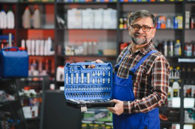 Kıdemli satıcı iyi organize edilmiş bir alet çantası tutuyor. Bir oto yedek parça mağazasında tüm prizler ve anahtarlarla dolu.