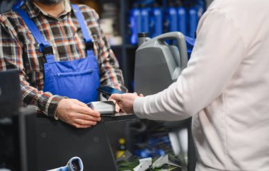 Müşteri oto yedek parça dükkanında araba yağını ödemek için akıllı telefon kullanıyor.