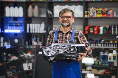 Gülümseyen satıcı oto yedek parça mağazasında yeni araba farı gösteriyor, yedek parça ve bakım kavramı