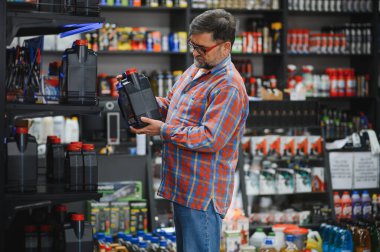 Tamirci oto yedek parça mağazasında motor yağını seçiyor, kırmızı kapaklı plastik şişede etiket okuyor