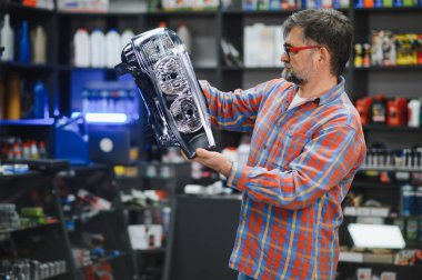 Oto yedek parça mağazasında müşteriye yeni bir araba farını sunan kıdemli satıcı, ürün seçimi konusunda uzman tavsiyesi ve yardım sunuyor