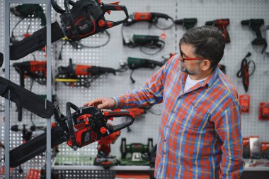 Müşteri bir hırdavatçıda elektrikli testere seçiyor, satılık çeşitli elektrikli aletleri ve ekipmanları inceliyor