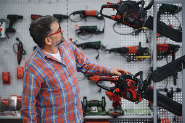 Müşteri hırdavatçı dükkanından elektrikli testereyi seçiyor. Satın almadan önce farklı model ve markaları değerlendiriyor.