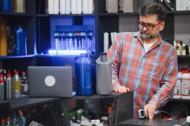 Satıcı kasada barkod tarayıcı kullanıyor, oto yedek parça mağazasında motor yağı ve diğer araba ürünleri satıyor.