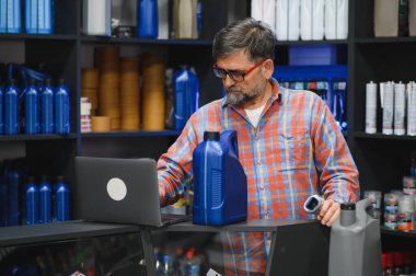 Bir oto yedek parça mağazasında motor yağı envanterini yöneten satıcı, raflardaki ürünleri düzenlemek için barkod tarayıcı ve dizüstü bilgisayar kullanıyor.