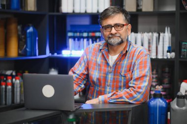 Satış elemanı dizüstü bilgisayarındaki siparişleri bir oto yedek parça mağazasında yönetiyor. Etrafı ürünlerle dolu.