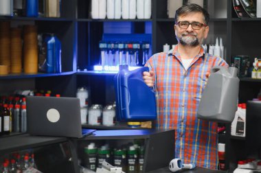 Satış elemanı iki motor yağı tenekesini bir oto yedek parça mağazasında dikilirken karşılaştırarak müşterilere ürün seçimi konusunda uzman tavsiyesi veriyor.