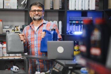 Bir oto yedek parça mağazasında çeşitli motor yağı şişelerini sergileyen satıcı, ürün seçimi ve bilgi ile müşterilere yardımcı oluyor