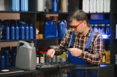 Kıdemli pazarlamacı, bir oto yedek parça mağazasında motor yağı şişeleriyle araçları seçiyor, profesyonel hizmet ve uzmanlık sağlıyor