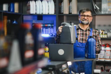Bir oto yedek parça mağazasında çeşitli motor yağı şişeleri sergileyen deneyimli bir satıcı, uzman danışmanlık ve hizmet sunan müşterilere yardımcı oluyor.