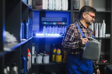 Satıcı, otomobil yedek parça mağazasında çalışırken elinde bir kutu motor yağı tutuyordu. Etrafı çeşitli araba ürünleriyle doluydu.