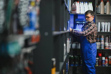 Oto yedek parça mağazasındaki motor yağı şişesine uzanan mavi giysili kıdemli satıcı.