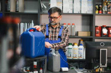 Bir oto yedek parça dükkanında çalışan satıcı büyük bir konteynırdan küçük bir konteynıra araba yağı döküyor.