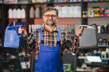 Bir oto yedek parça mağazasında müşterilere yardım ederken iki kutu motor yağı tutan tamirci, otomotiv bakımı alanında uzmanlık gösteriyor