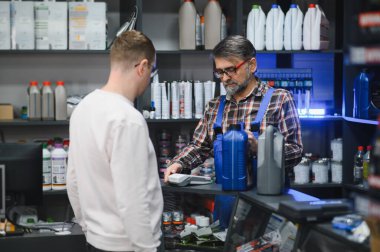 İşlek bir oto yedek parça mağazasında müşteriye satın almalarında yardımcı olurken çeşitli motor yağlarını tutuyor ve sergiliyor