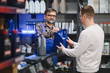 Tamirci oto yedek parça dükkanındaki müşteriye motor yağı veriyor. Her ikisi de araba yağı dolu bir teneke kutu taşıyor.