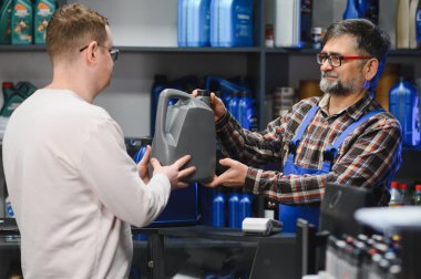 Bir oto yedek parça mağazasında tamircinin müşteriye araba yağı vermesi, araç bakımı için profesyonel tavsiyeler ve kaliteli ürünler sunması