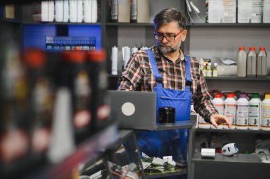Kıdemli satıcı, oto yedek parça mağazasında çalışırken dizüstü bilgisayar kullanarak envanteri kontrol edip siparişleri yönetir.