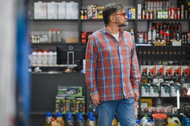 Bir oto yedek parça mağazasında kıdemli satıcı, raflardaki ürünlere bakıyor, müşteri hizmetleri ve uzmanlık sağlıyor.