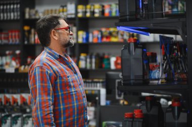 Tamirci, otomobil yedek parça mağazasında raflara göz atarken motor yağı seçiyor ve en uygun araba bakımı için çeşitli ürünleri inceliyor