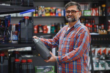 Bir oto yedek parça mağazasında satış elemanı motor yağını tutuyor ve kontrol ediyor. Müşterisi için doğru ürünü seçiyor.