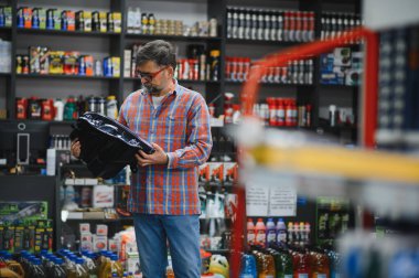 Tamirci bir oto yedek parça mağazasından araba parçası seçiyor, yedek parça tutuyor ve kalitesini kontrol ediyor.