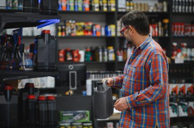 Oto yedek parça mağazasında müşteriler motor yağı şişesini tutuyor ve satın alma konusunda karar veriyor.