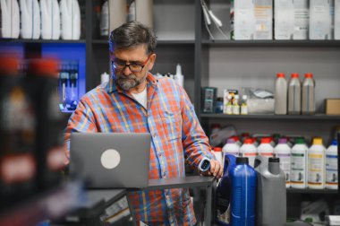 Satış elemanı otomobil parçaları mağazasında çalışırken dizüstü bilgisayar kullanıyor ve barkod tarayıcı tutuyor, envanter ve müşteri siparişlerini kontrol ediyor