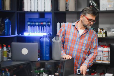 Kasada barkod tarayıcı kullanan kıdemli bir satıcı, araba ürünleri ve araç yedek parça mağazasında malzemelerle çevrili.
