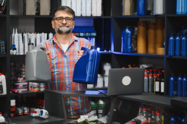 Satıcının elinde iki kutu motor yağı var. Oto yedek parça mağazasındaki müşterilere ürünleri sunuyor.