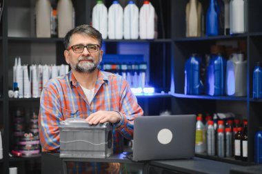 Kıdemli satıcı yeni araba aküsünü bir oto yedek parça mağazasında dizüstü bilgisayarla sunuyor.