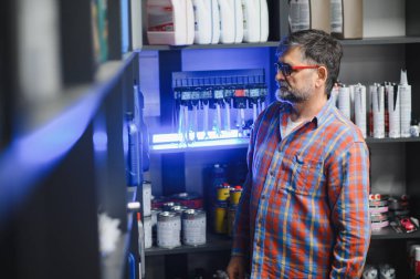 Satış elemanı iyi stoklanmış bir oto yedek parça mağazasına göz atıyor, motor yağı ve bakım ve onarım ihtiyaçları için çeşitli araba ürünleri seçiyor