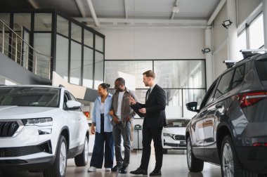 Araba satıcısı, modern otomobil bayiliğinde Afro-Amerikan çifte yeni araç özellikleri gösteriyor. Satın alma seçenekleri ve finansman konularını tartışıyorlar.