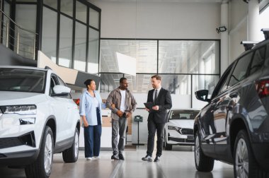 Satıcının elinde bir dosya var. Parlak ve geniş bir galeriyi gezerken Afro-Amerikan bir çifte yeni arabaları sunuyor.