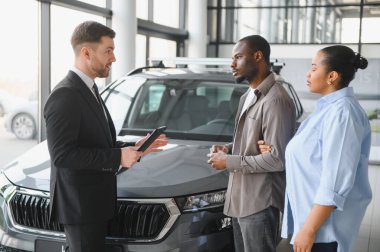 Araba satıcısı Afrika kökenli Amerikalı çifte yeni araba sunuyor. Modern otomobil galerisindeki özellikleri ve satın alma seçeneklerini tartışıyorlar.