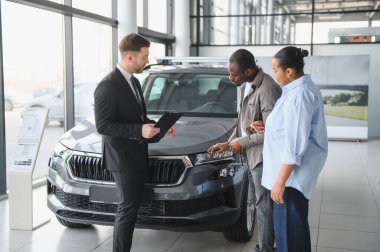 Modern bir galeride araba almak isteyen Afro-Amerikan bir çifte yeni bir arabanın özelliklerini gösteren profesyonel bir araba satıcısı.