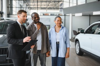 Araba satıcısı, modern otomobil bayiliğinde el ele tutuşan Afrikalı Amerikalı bir çifte araç satın alma anlaşmasını anlatıyor.