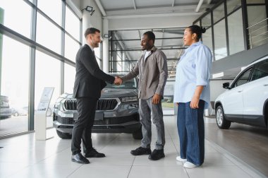Araba galerisinde bir müşteriyle tokalaşan satıcı, yeni bir araba alımını sonuçlandırıyor.
