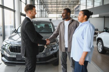 Satıcı, Afro-Amerikan bir çiftle el sıkışıyor ve aceleci bir galeride yeni bir araba alımına son veriyor.