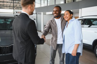 Gülümseyen çift, galeriden yeni bir araba alırken bir satıcıyla tokalaşırken heyecan ve memnuniyet saçar.