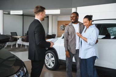 Mutlu çift yeni bir araba alırken bir satıcıyla takılıyor, anahtarlarını tutuyor ve canlı bir galeride seçenekleri tartışıyor.