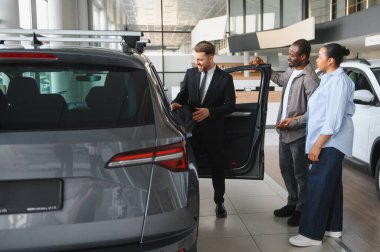 Araba satıcısı, bir araba galerisinde Afro-Amerikan bir çifte yeni bir arabanın özelliklerini gösteriyor.