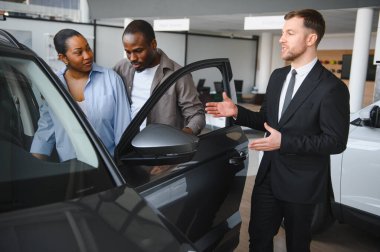 Araba satıcısı, Afrikalı Amerikalı bir çifte yeni bir arabanın özelliklerini sunuyor. Modern bir bayilikte bilinçli bir karar vermelerine yardımcı oluyor.