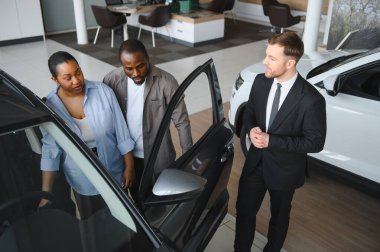 Araba satıcısı, bir galeride bir çifte yeni bir araba sunuyor. Özellikleri ve satın alma seçeneklerini tartışıyor.