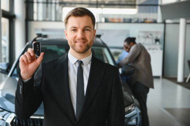 Araba satıcısı, müşteriler lüks bir galeride ideal otomobillerini seçerken yeni araba anahtarını sunuyor.