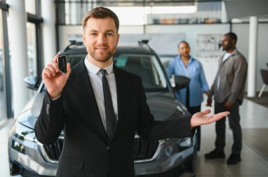 Araba satıcısı araba anahtarlarını gösteriyor ve bir araba galerisinde Afro-Amerikan bir çifte yeni bir araç sunuyor.