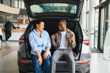 Heyecanlı çift yeni arabalarının bagajında oturmuş, bir galeride gülümsüyor, konuşuyor, alışverişlerinin tadını çıkarıyorlar.